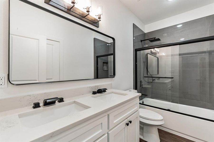 Full bathroom with bath / shower combo with glass door, wood-type flooring, vanity, and toilet