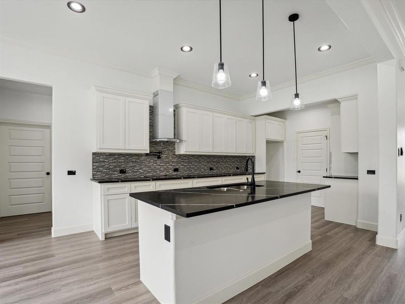 Kitchen with light hardwood / wood-style flooring, white cabinets, wall chimney range hood, and backsplash