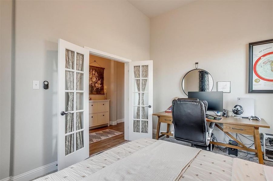 Home office with wood-type flooring, a towering ceiling, and french doors