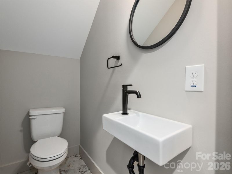 Lower-level half bath with pedestal sink, ceramic tile flooring, and clean modern finishes.