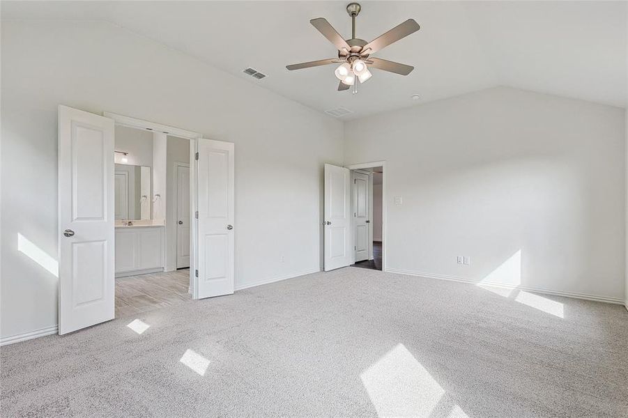 Unfurnished bedroom with ceiling fan, light colored carpet, connected bathroom, and vaulted ceiling