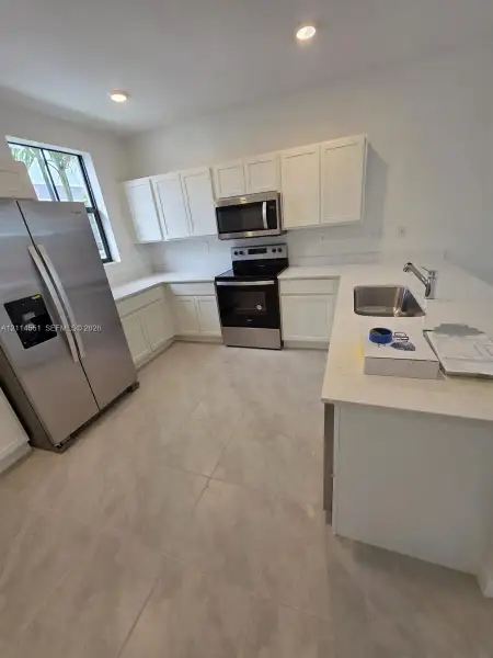 Kitchen featuring white shaker-style cabinetry, quartz countertops, stainless steel appliances, a peninsula with an undermount sink, and neutral tile flooring
