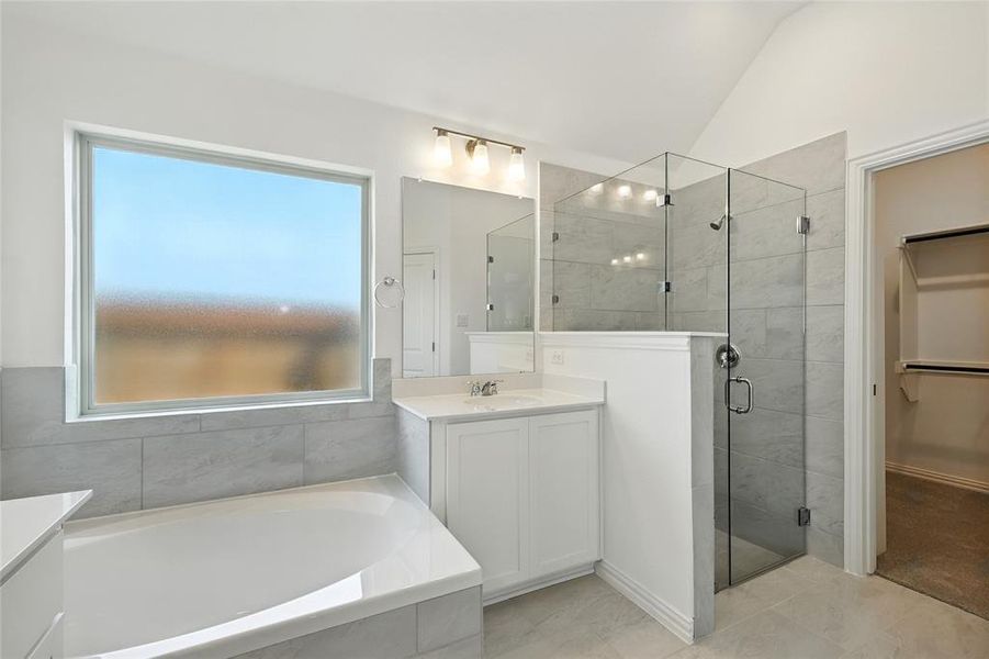 Full bath with a stall shower, vanity, a garden tub, lofted ceiling, and a spacious closet