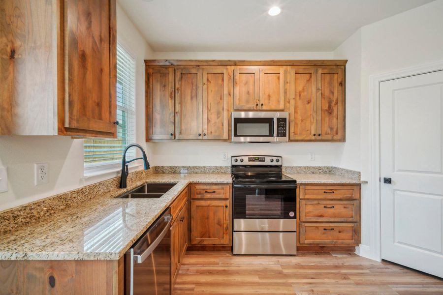 Kitchen featuring brown cabinetry, light stone countertops, a sink, light wood-style floors, and appliances with stainless steel finishes