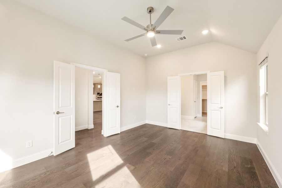 Empty bedroom with dark hardwood floors, vaulted ceiling, ceiling fan, and doors leading to a closet and hallway. Empty bedroom with dark hardwood floors, vaulted ceiling, ceiling fan, and doors leading to a closet and hallway.