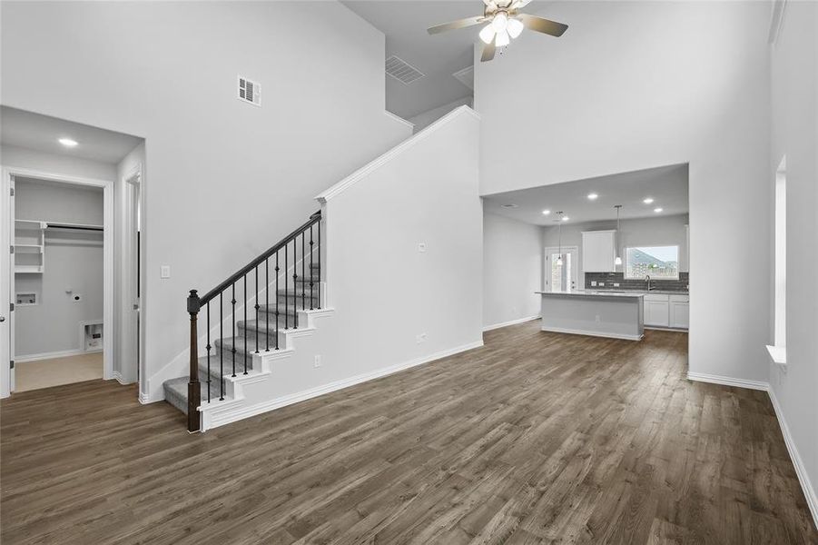 Unfurnished living room featuring a towering ceiling, stairs, dark wood finished floors, a ceiling fan, and recessed lighting