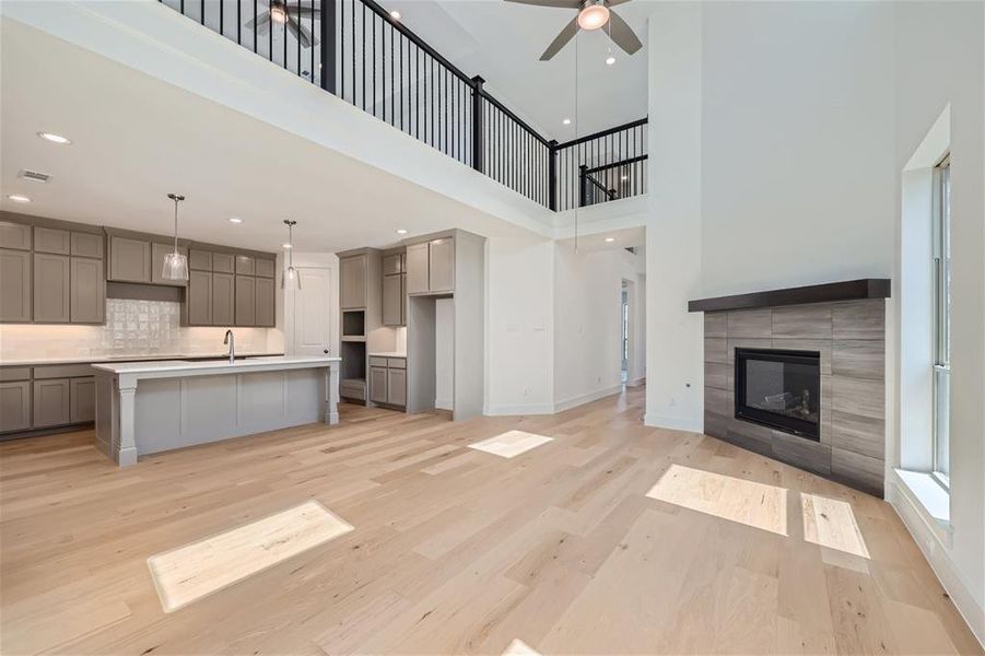 Kitchen with light wood-type flooring, ceiling fan, a fireplace, decorative light fixtures, and a center island with sink