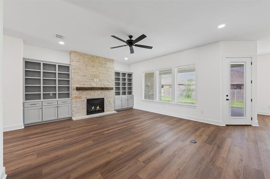 Living room with wood-look flooring, a stone fireplace with a wooden mantel, and built-in shelving units