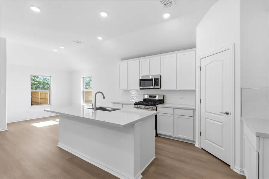 Kitchen with backsplash, white cabinets, a center island with sink, light wood finished floors, and recessed lighting Kitchen with backsplash, white cabinets, a center island with sink, light wood finished floors, and recessed lighting
