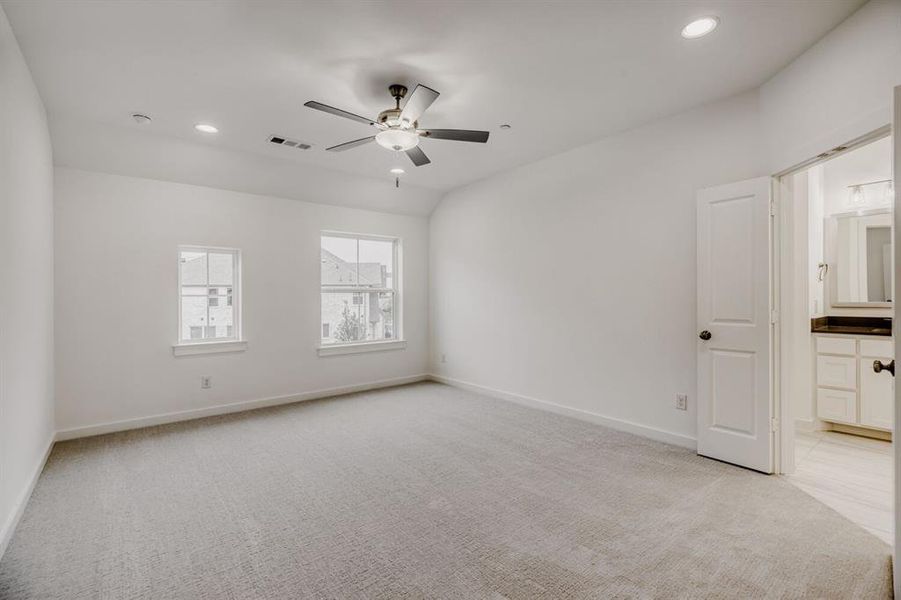 Spacious room featuring light-toned carpet flooring, two windows, and a ceiling fan with integrated lighting