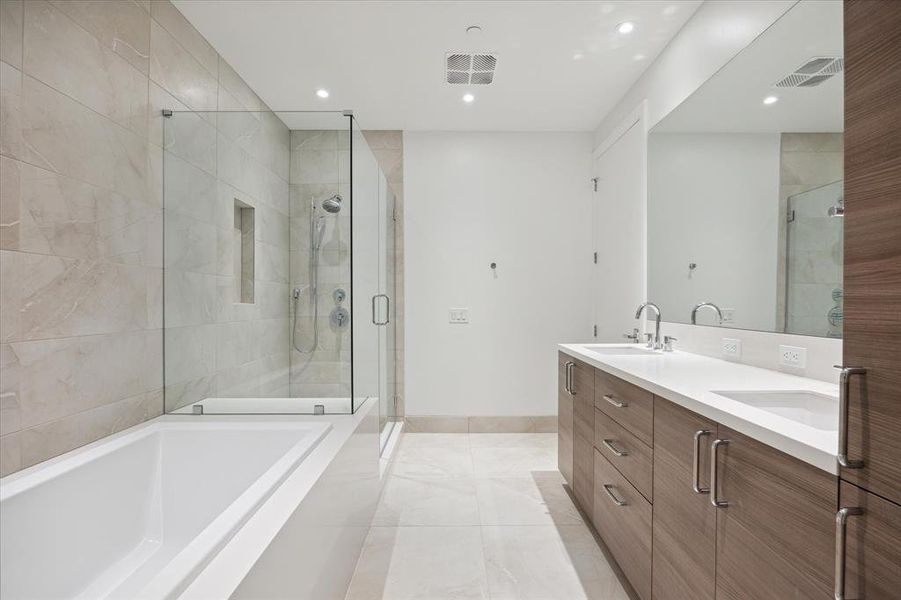 Primary bathroom suite featuring a double vanity with ample counter & storage space, a large expansive mirror, a walk-in shower with bench, frameless glass enclosure, and separate soaking bathtub.