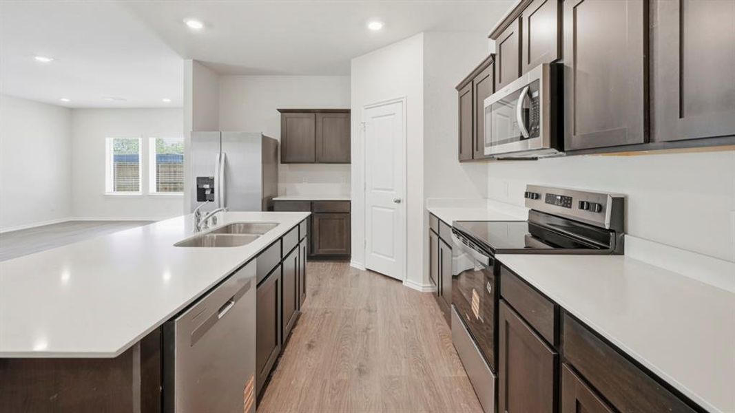 Kitchen featuring appliances with stainless steel finishes, light wood-style flooring, dark brown cabinets, and recessed lighting