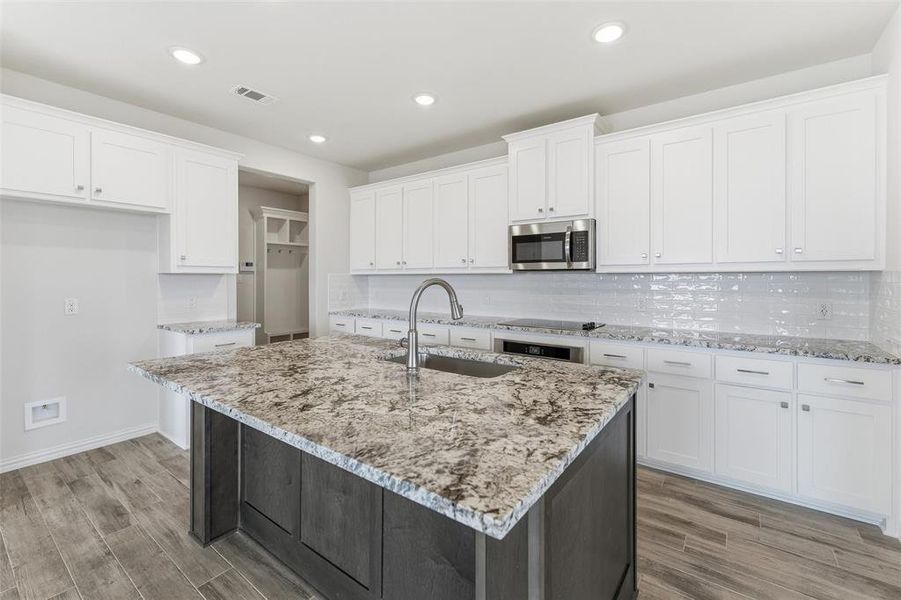Two tone kitchen with two tone color scheme, light wood-style flooring, a center island with sink, stainless steel appliances, and tasteful backsplash