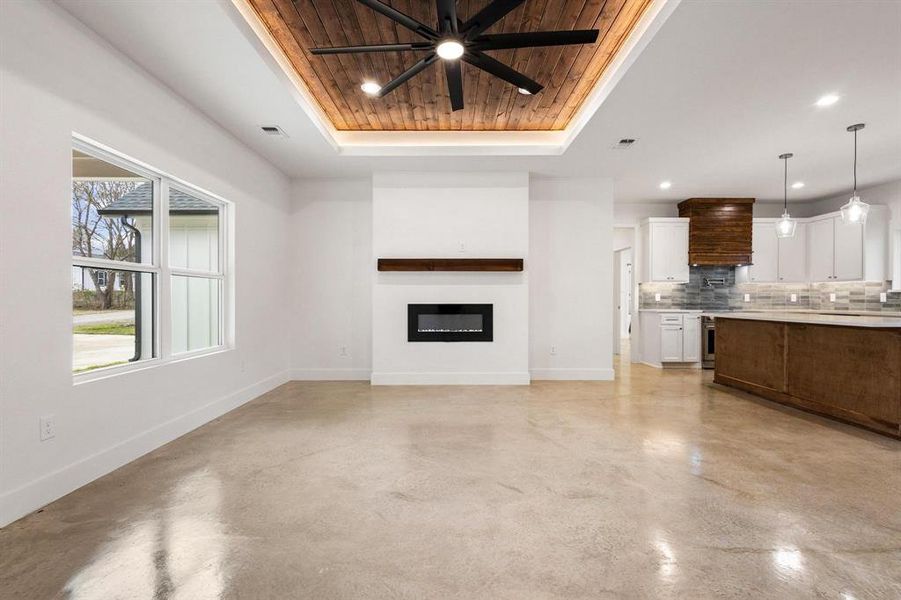 Unfurnished living room with wooden ceiling, a glass covered fireplace, ceiling fan, concrete flooring, and a raised ceiling