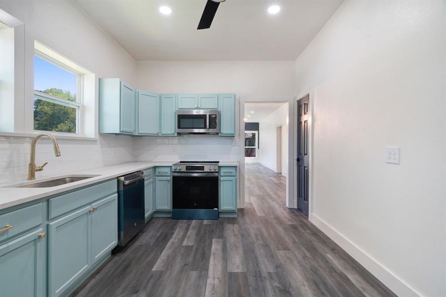 Kitchen with ceiling fan, tasteful backsplash, blue cabinets, stainless steel appliances, and dark wood-style flooring Kitchen with ceiling fan, tasteful backsplash, blue cabinets, stainless steel appliances, and dark wood-style flooring