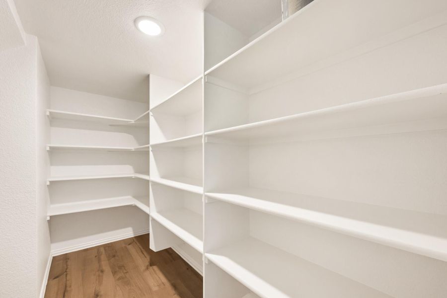 Walk-in pantry with white built-in shelves on three walls and hardwood floors