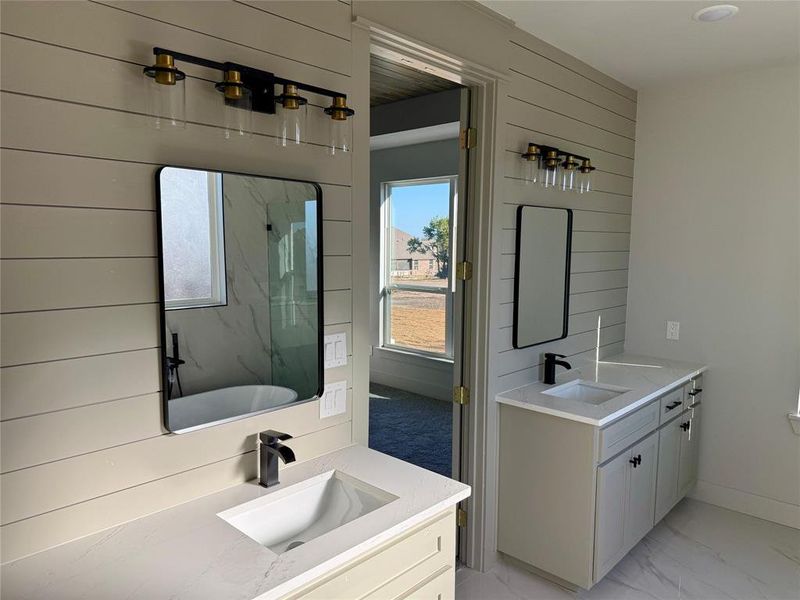 Full bath with two vanities, light marble finish floors, a marble finish shower, wood walls, and a soaking tub