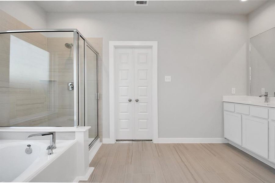 The expansive walk-in shower surrounded with tile and the distinct garden tub adorned with unique details will enhance your daily rituals at the sophisticated vanity, featuring double sinks, light-colored countertops, contemporary hardware, and exquisite vanity lights.  Sample photo of completed home with similar plan. As built color and selections may vary.