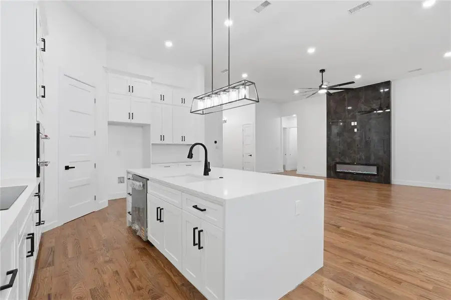 Kitchen with a center island with sink, open floor plan, light stone counters, white cabinetry, and pendant lighting