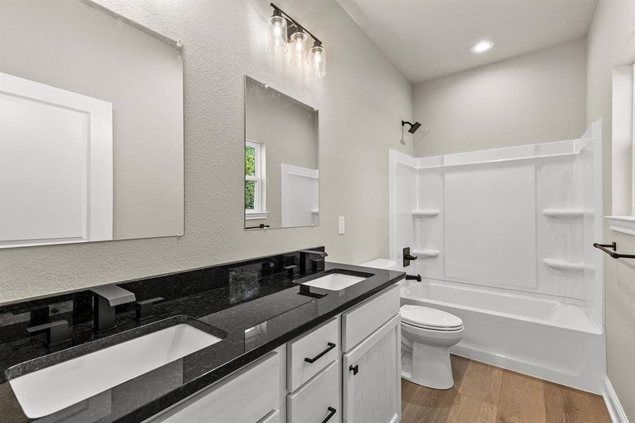 Full bathroom with shower / bath combination, light wood-style floors, double vanity, and a textured wall Full bathroom with shower / bath combination, light wood-style floors, double vanity, and a textured wall