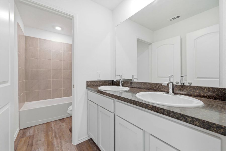 Upstairs full bath with double sinks, shaker cabinets, vinyl plank floors, and a relaxing tub/shower combo—functional style for the family.