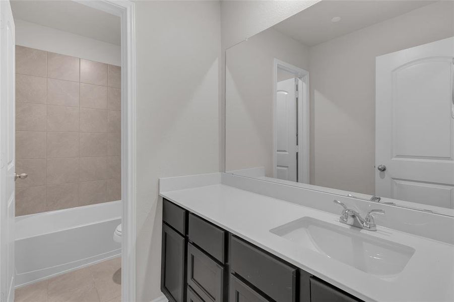 This is a modern bathroom featuring a large vanity with a dual sink, ample storage in dark cabinetry, and a full bathtub with tile surround. The space is clean and well-lit, with neutral colors.