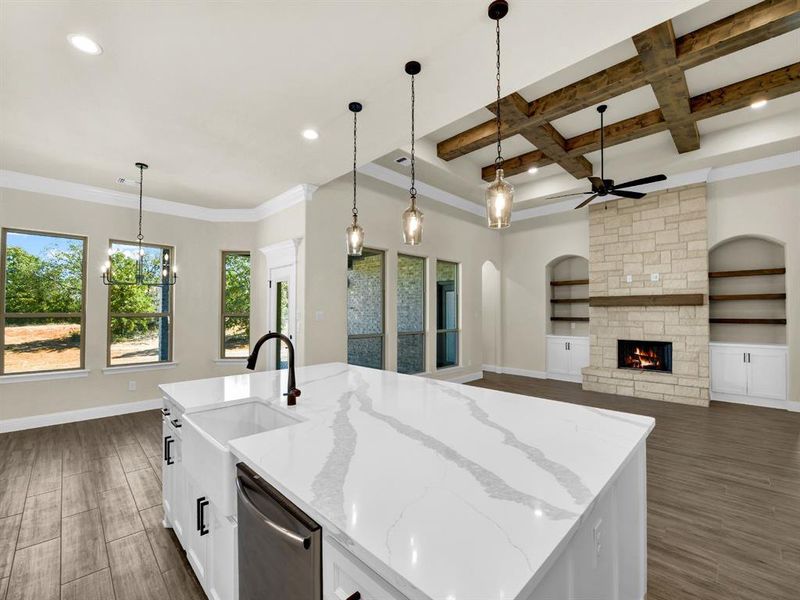 Kitchen with light stone countertops, stainless steel dishwasher, coffered ceiling, white cabinets, and an island with sink