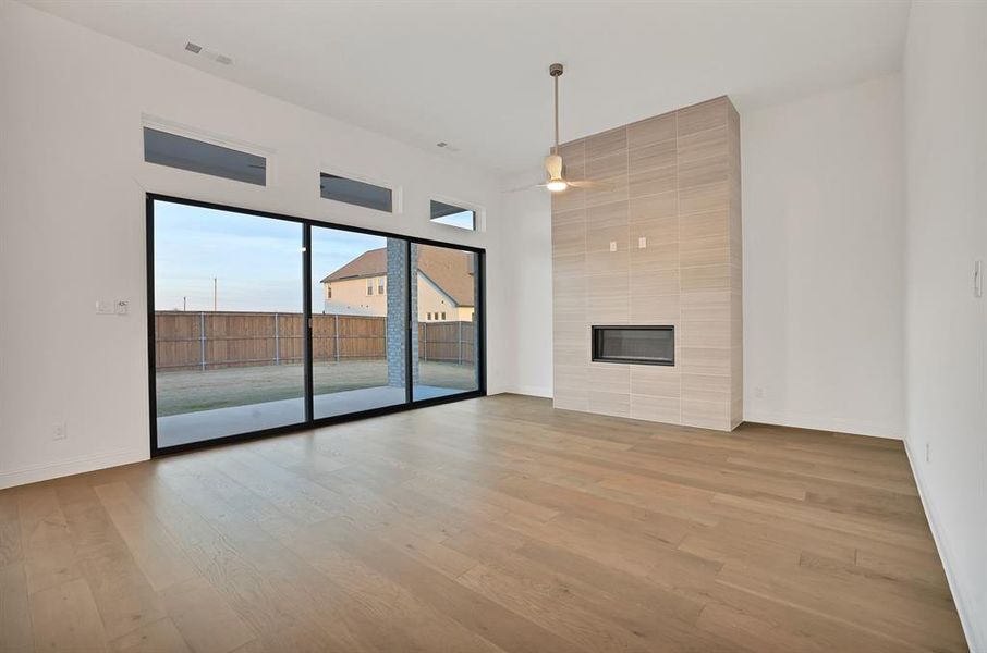 Living room with ceiling fan, a tiled fireplace, and wood-type flooring