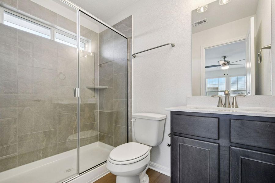Full bathroom featuring a shower stall, vanity, a textured wall, and a ceiling fan