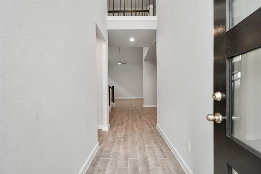 The grand entrance beckons with high ceilings, adorned with elegant wood-look tile flooring and oversized baseboards.  Sample photo of completed home with similar floor plan. As-built interior colors and selections may vary.