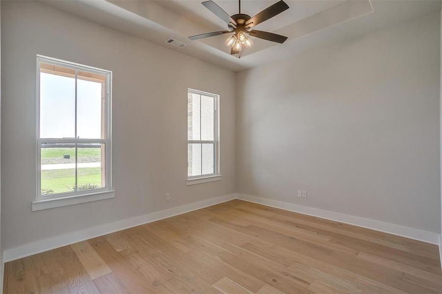 Unfurnished room with visible vents, baseboards, a raised ceiling, and light wood finished floors Unfurnished room with visible vents, baseboards, a raised ceiling, and light wood finished floors