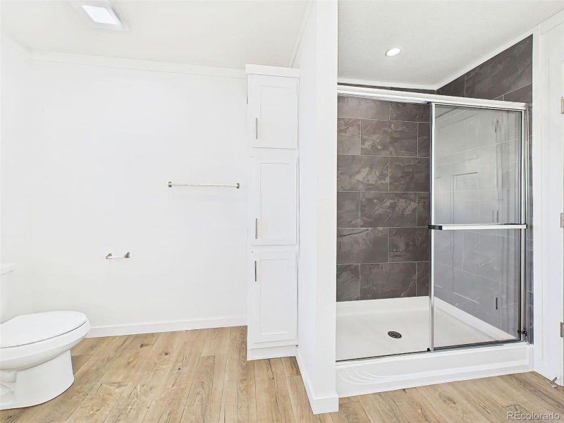 A sleek glass-enclosed shower with modern tile surround complements the built-in linen storage and clean white finishes.