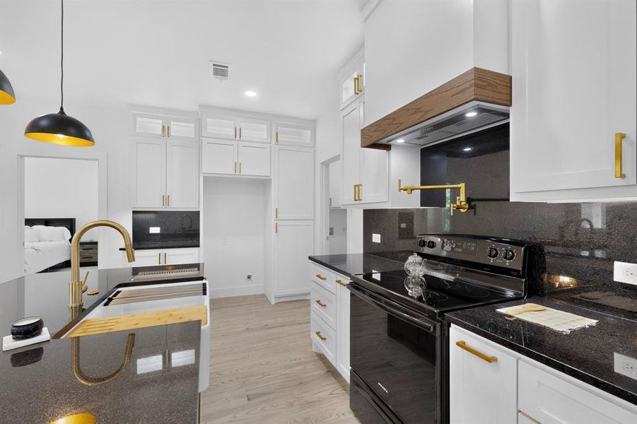 Contemporary kitchen featuring white cabinetry with gold-tone hardware, dark countertops, and light wood-finish flooring