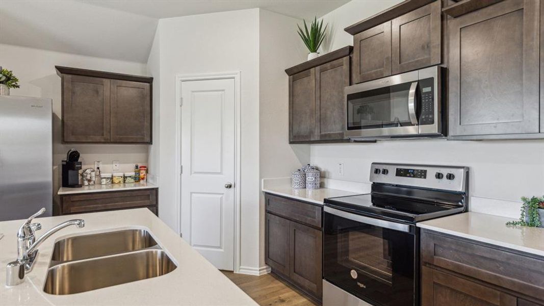 Kitchen featuring stainless steel appliances, dark wood finish cabinets, light wood finished floors, and light stone countertops