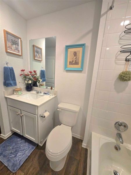 Bathroom featuring a white vanity with an integrated sink, polished chrome fixtures, a white toilet, and wood-finish flooring