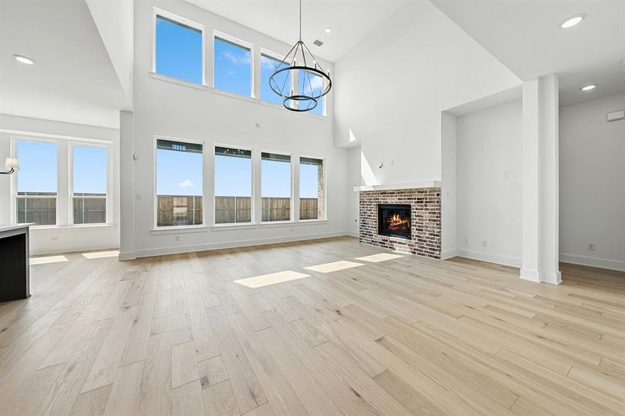Unfurnished living room featuring a chandelier, recessed lighting, a brick fireplace, light wood finished floors, and a towering ceiling