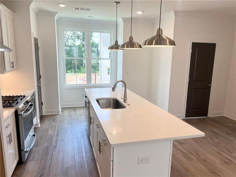 Kitchen featuring gas stove, an island with sink, dark wood-type flooring, ornamental molding, and white cabinets