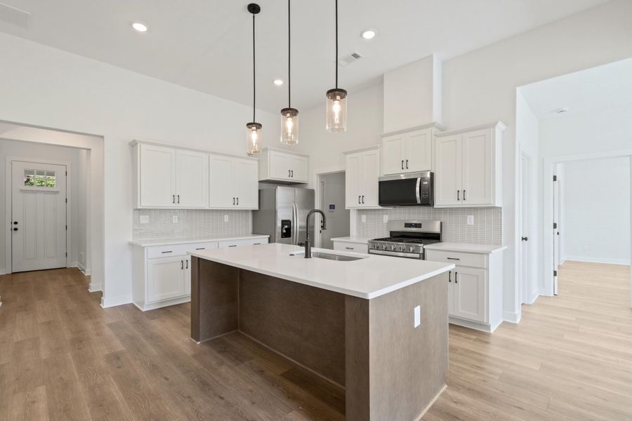 Kitchen featuring a central island with white countertop, white cabinetry with dark hardware, stainless steel appliances, and wood-finish flooring Kitchen featuring a central island with white countertop, white cabinetry with dark hardware, stainless steel appliances, and wood-finish flooring