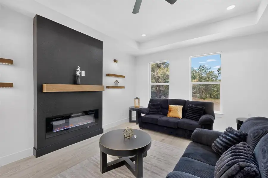 Living area featuring a modern black fireplace wall with a wood mantel, an electric firebox, and integrated floating shelves