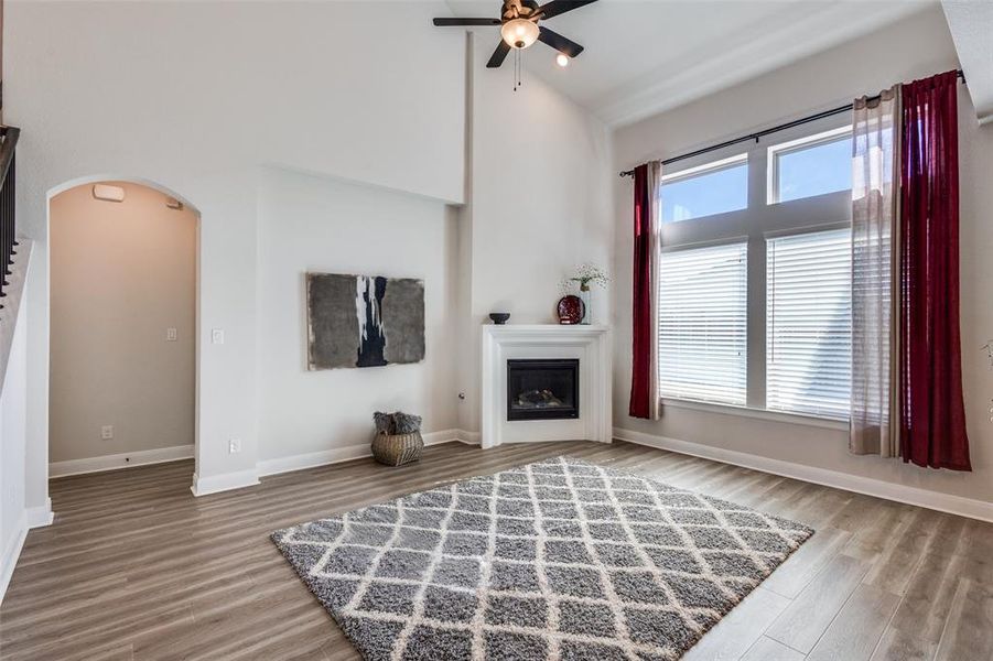 Unfurnished living room featuring arched walkways, a glass covered fireplace, light wood-type flooring, ceiling fan, and a high ceiling