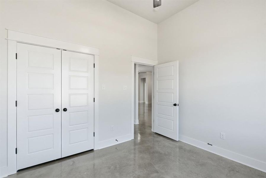 Unfurnished bedroom featuring finished concrete floors, a high ceiling, a closet, and ceiling fan