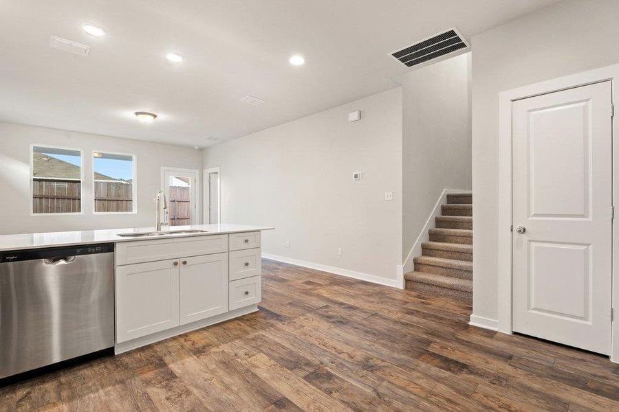 Kitchen with stainless steel dishwasher, dark wood finished floors, white cabinetry, recessed lighting, and light stone counters