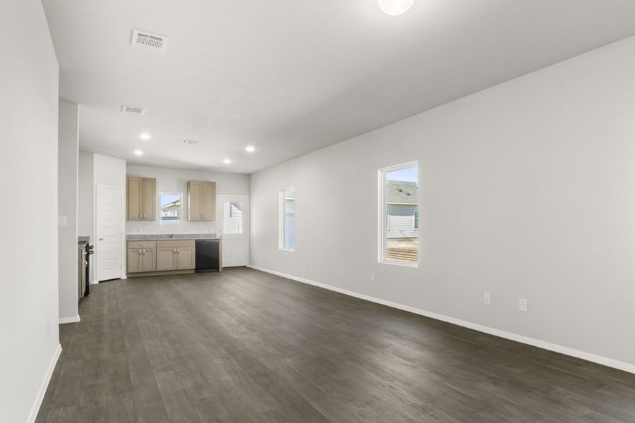 Image of a living room with dark brown vinyl, light grey walls, windows and a open kitchen in the distance