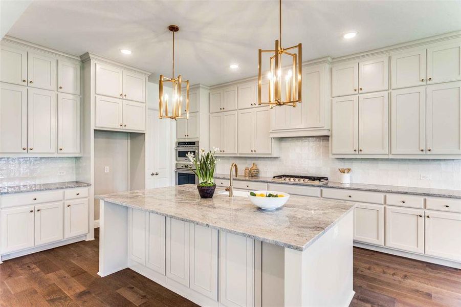 Kitchen featuring backsplash, light stone counters, dark wood finished floors, hanging light fixtures, and an island with sink Kitchen featuring backsplash, light stone counters, dark wood finished floors, hanging light fixtures, and an island with sink