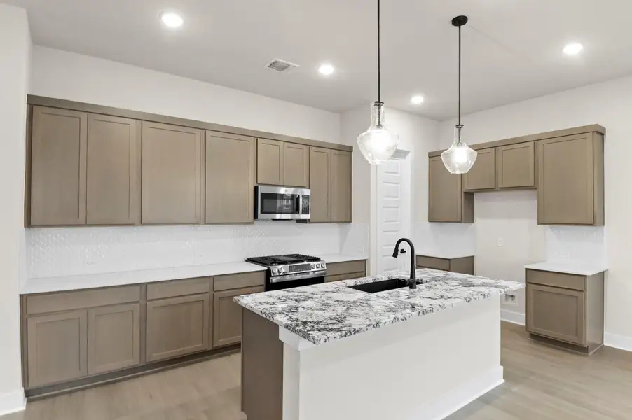 Kitchen featuring tasteful backsplash, light stone counters, pendant lighting, stainless steel appliances, and a kitchen island with sink