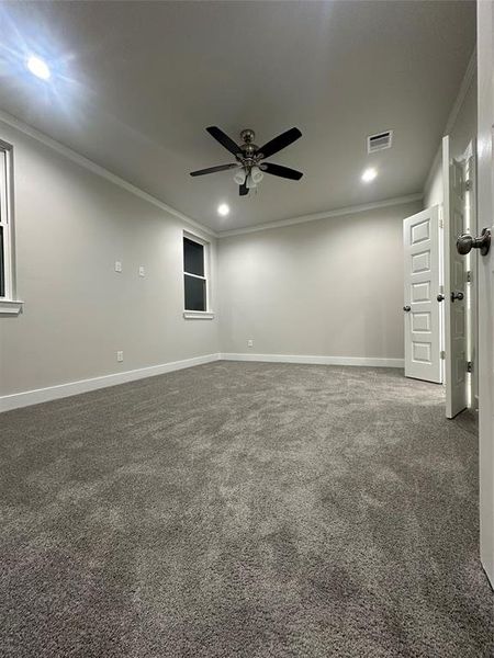 Empty room featuring ceiling fan, ornamental molding, and dark colored carpet