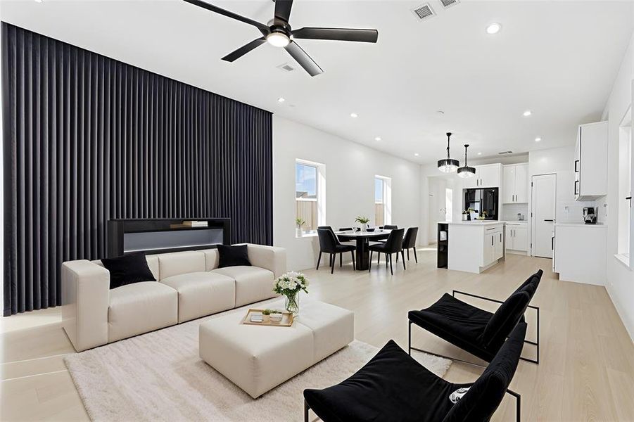 Open-concept living space featuring light wood-finish flooring, recessed lighting, and a modern black slatted accent wall with an integrated linear electric fireplace