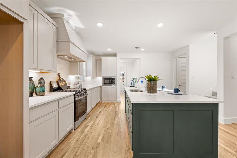Kitchen with stainless steel appliances, light wood-style flooring, a center island with sink, decorative backsplash, and recessed lighting
