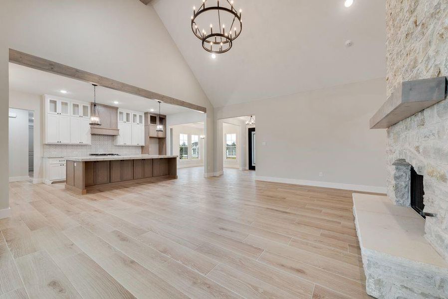 Unfurnished living room featuring high vaulted ceiling, a fireplace, an inviting chandelier, and light hardwood / wood-style flooring