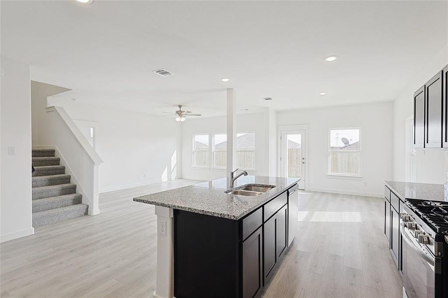 Kitchen with light stone countertops, sink, stainless steel appliances, light hardwood / wood-style flooring, and a center island with sink